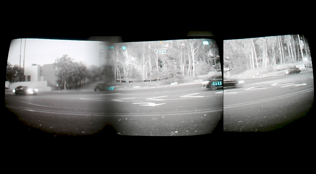 A quad pano night vision view from inside a vehicle showing a road intersection with trees, cars, and traffic lights, framed by a dark border.